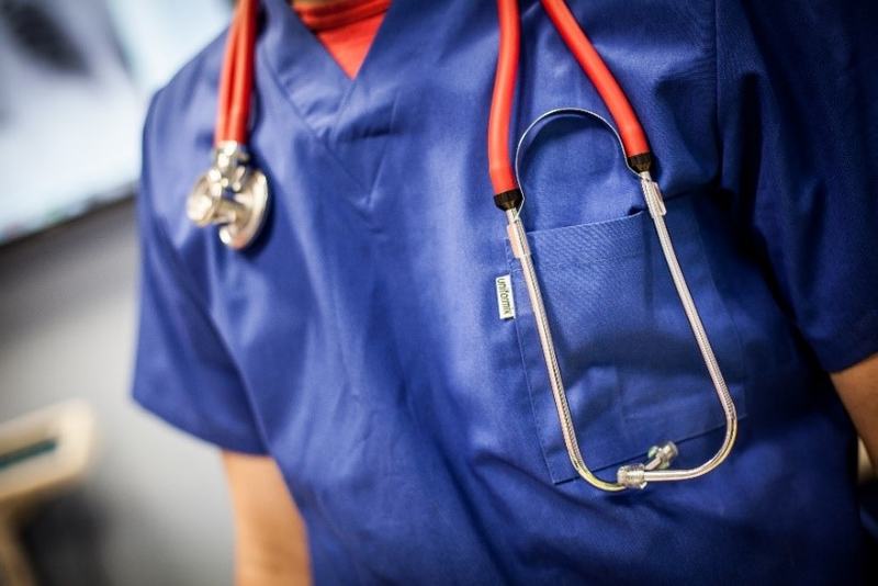 Zbliżenie na niebieską bluzę medyczną z czerwonym stetoskopem zawieszonym na szyi i włożonym do kieszeni