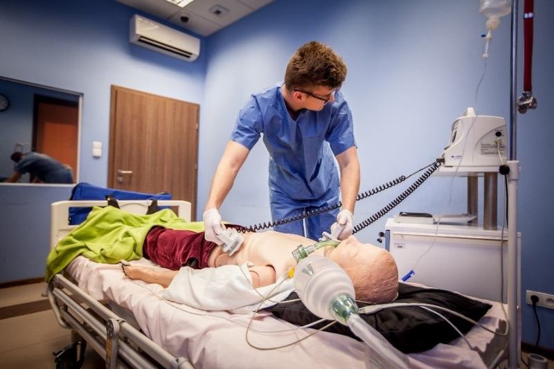 Student medycyny w niebieskim stroju operacyjnym przykłada łyżki defibrylatora do klatki piersiowej fantomu medycznego