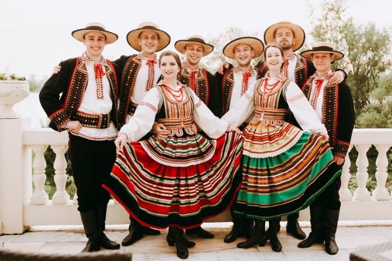 Grupa tancerzy zespołu ludowego w tradycyjnych, wielobarwnych strojach ludowych i słomkowych kapeluszach pozuje na tarasie